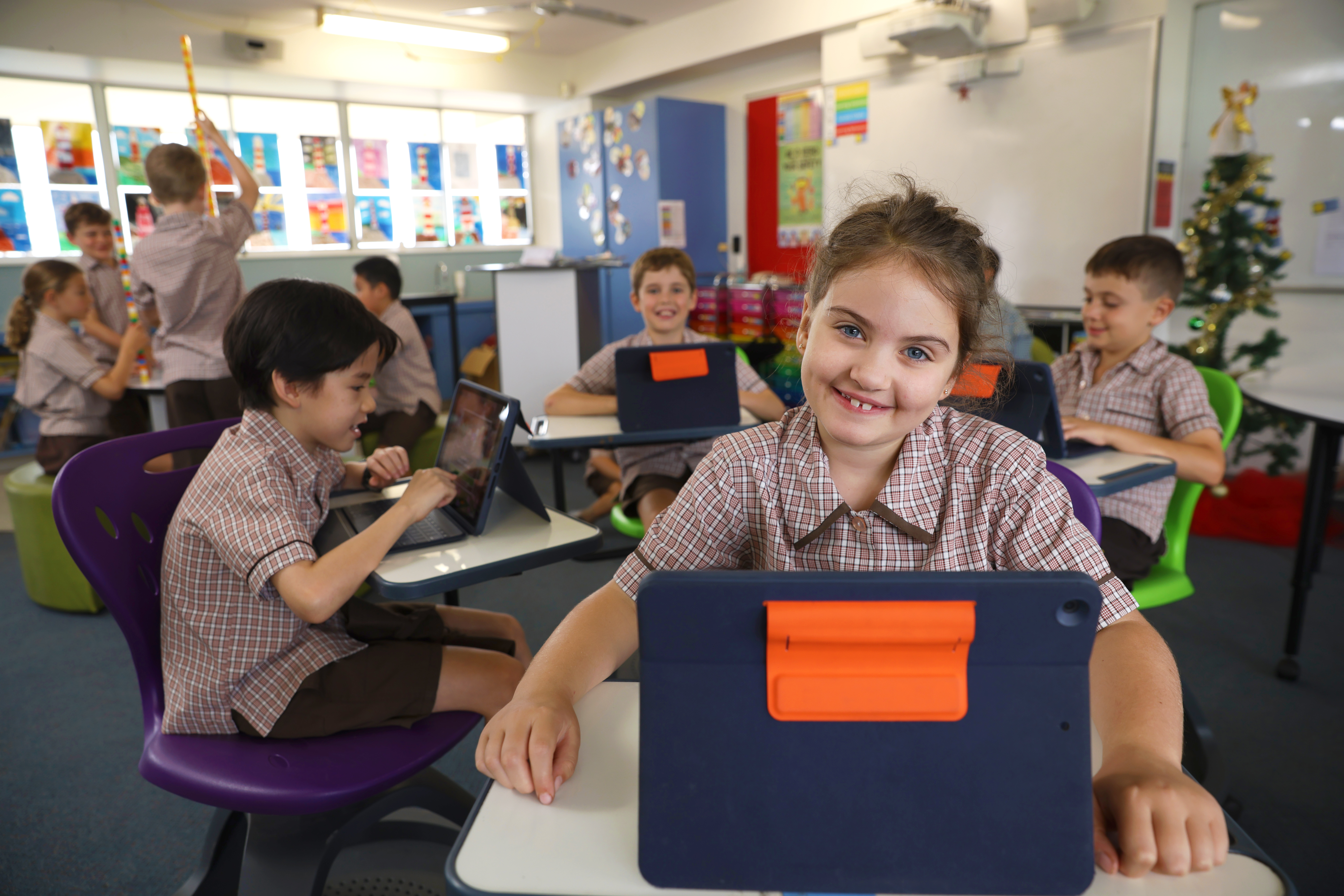 Students in school uniform sitting at desks using tablets during a classroom learning activity.